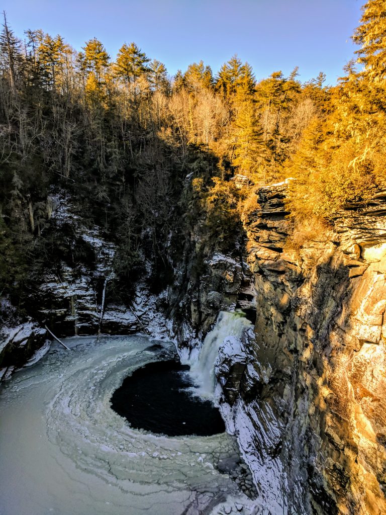 frozen pool with waterfall pouring in from above mountain cliff
