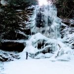 large frozen waterfall in the woods with woman standing in front looking up