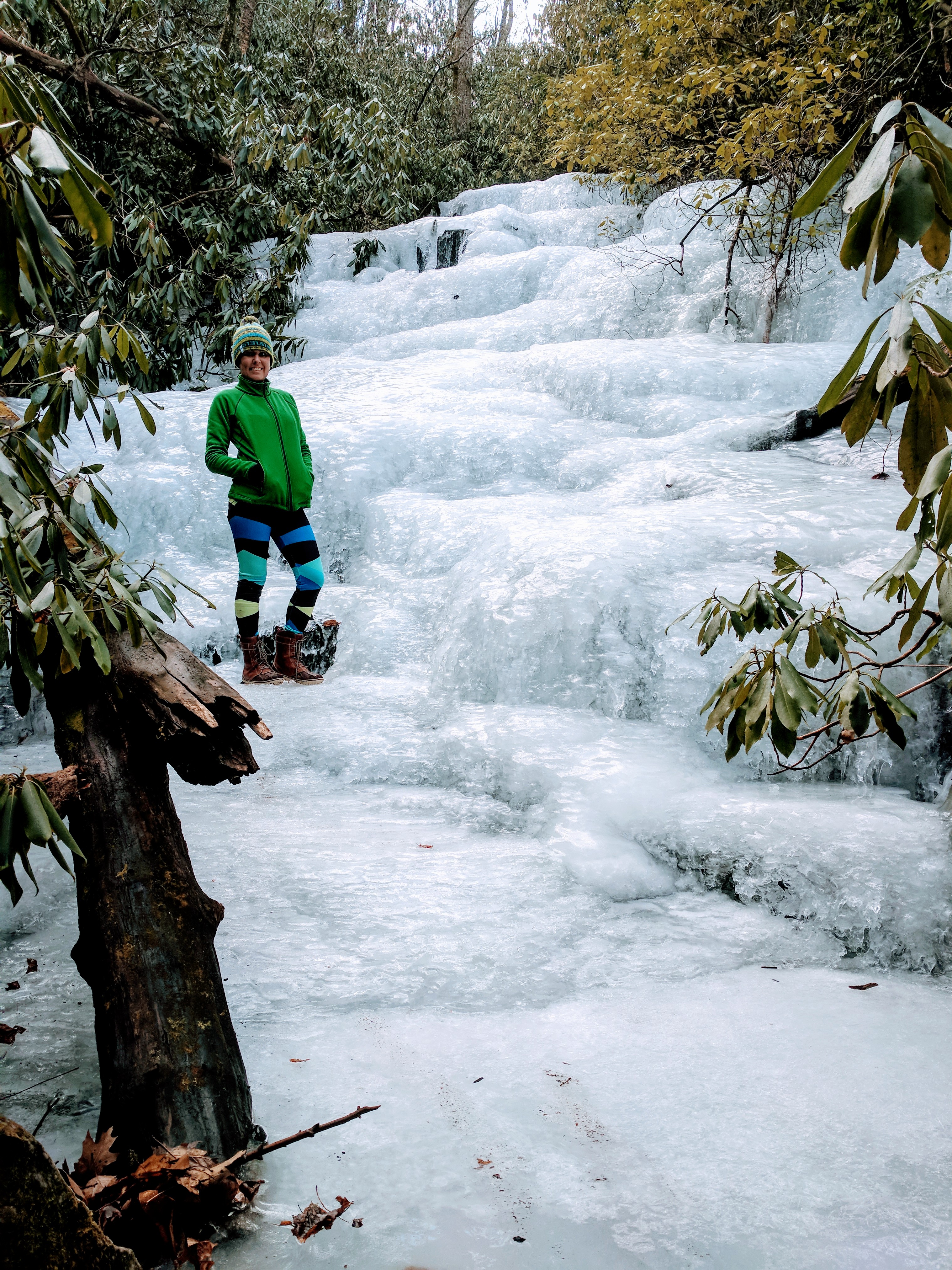 frozen meandering waterfall with woman in green jacket and hat standing on ice