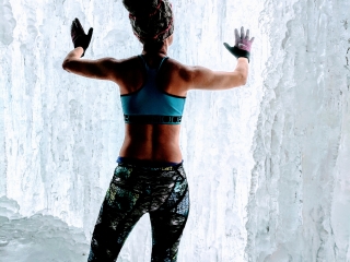 woman in ice cave touching frozen wall wearing workout clothes
