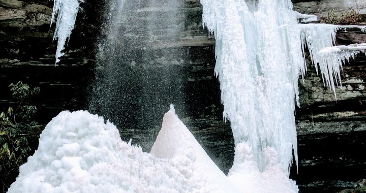 woman holding blocks of ice at bottom of a freezing waterfall