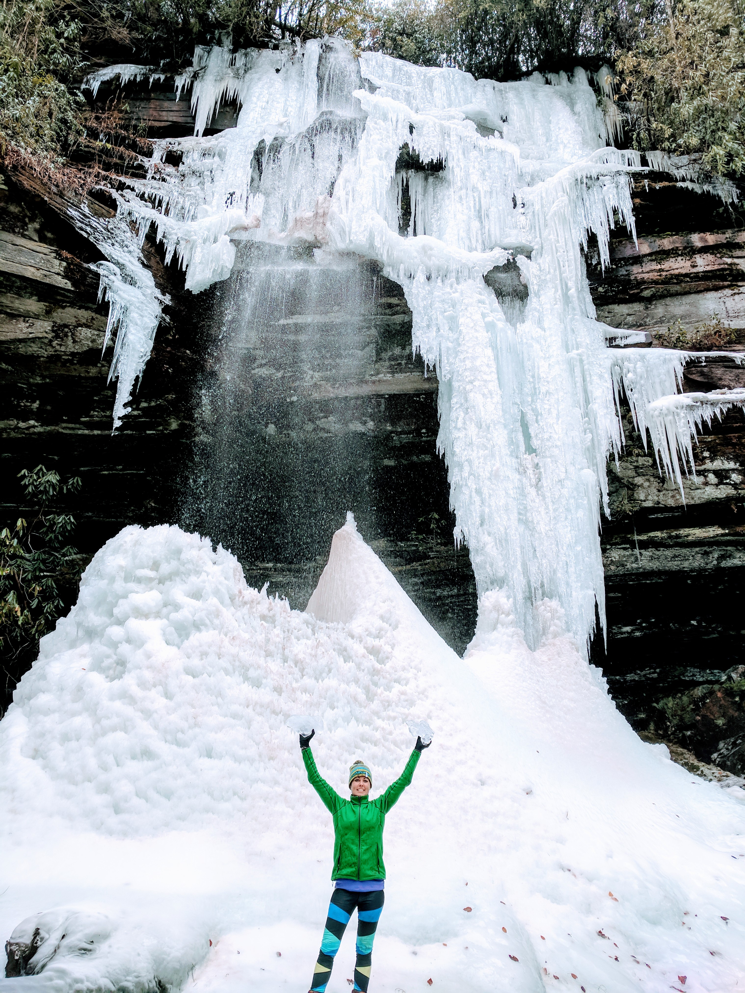 woman holding blocks of ice at bottom of a freezing waterfall