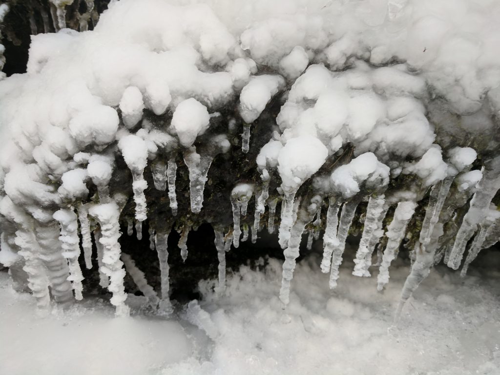 icicles with snow attached to them form on the edge of overhanging rocks