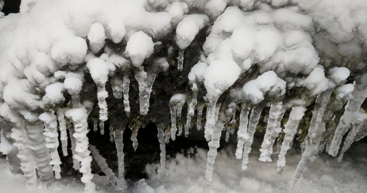 icicles with snow attached to them form on the edge of overhanging rocks